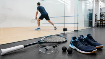 Squashketcher, briller, sko og bolde ved en squashbane